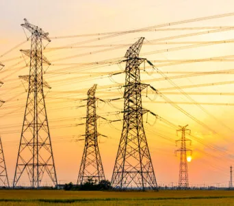 high-voltage power lines at sunset, high voltage electric transmission tower. Symbolizing power infrastructure and energy market evaluation.